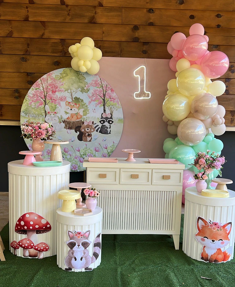 Painel de bosque com raposa e coelhos, balões em tons pastel e cômoda branca com doces
