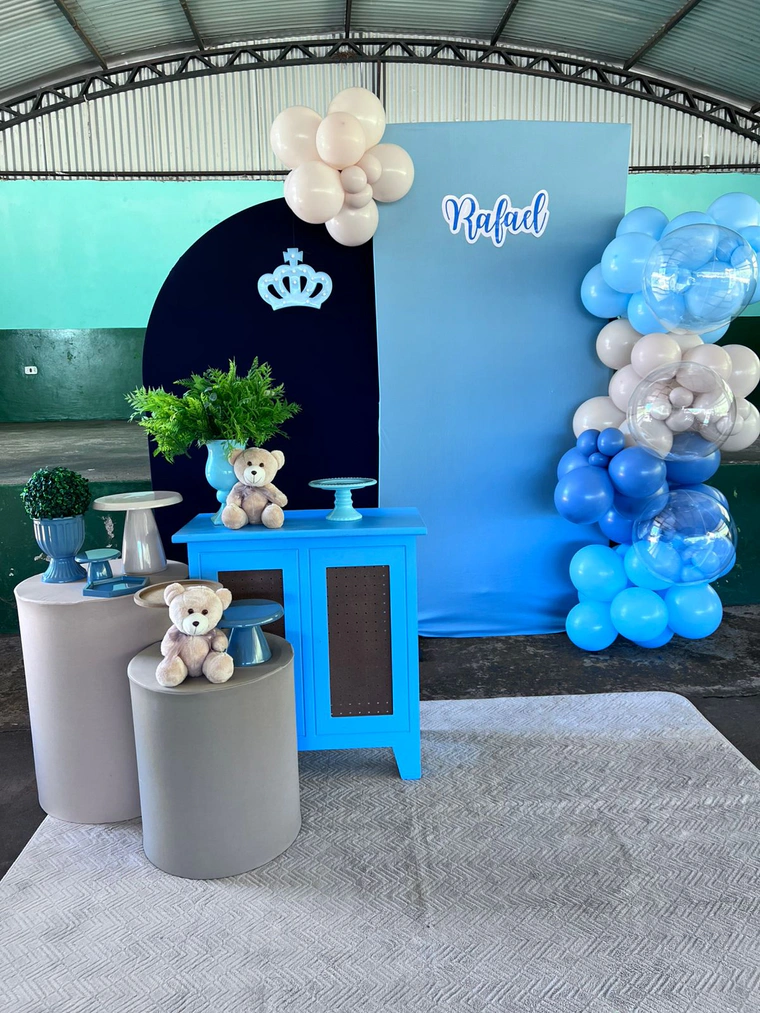Painel azul com coroa e ursinhos de pelúcia, arco de balões azuis e cômoda azul