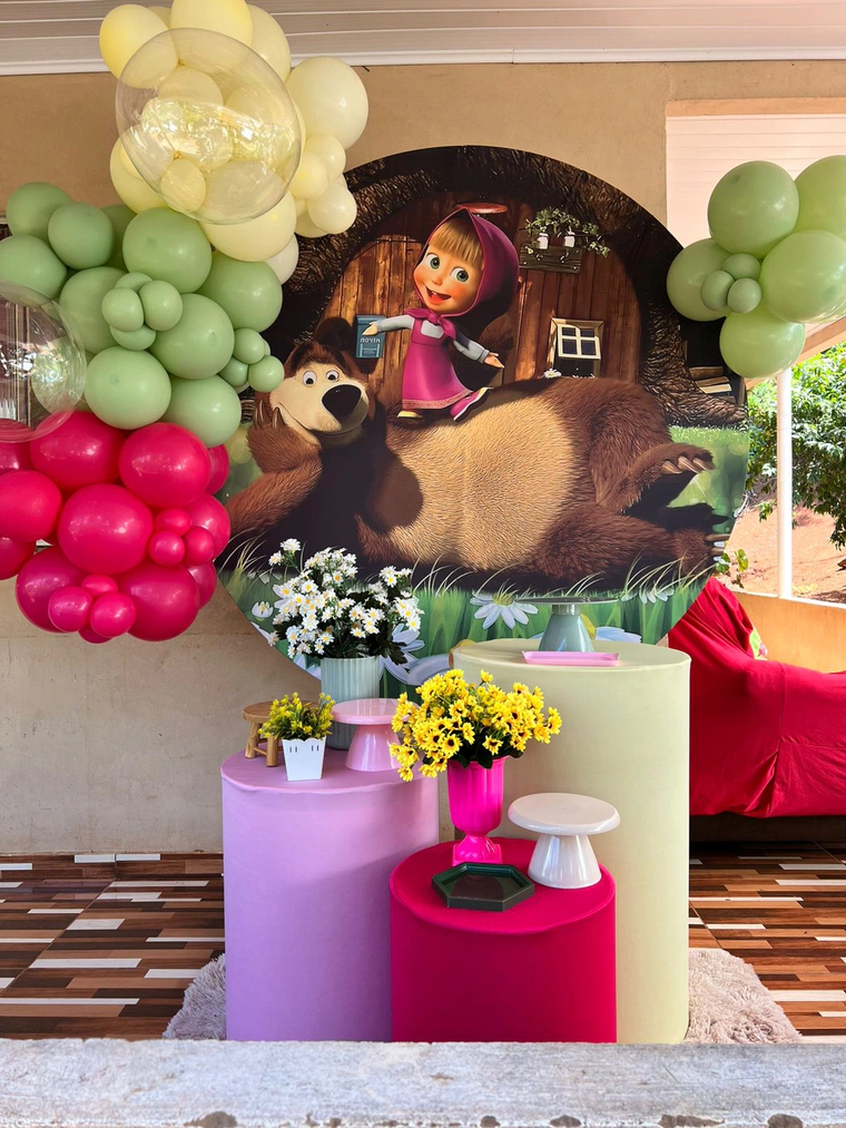 Painel redondo da Masha com arco de balões verdes, amarelos e pink, e mesas de bolo em rosa e lilás