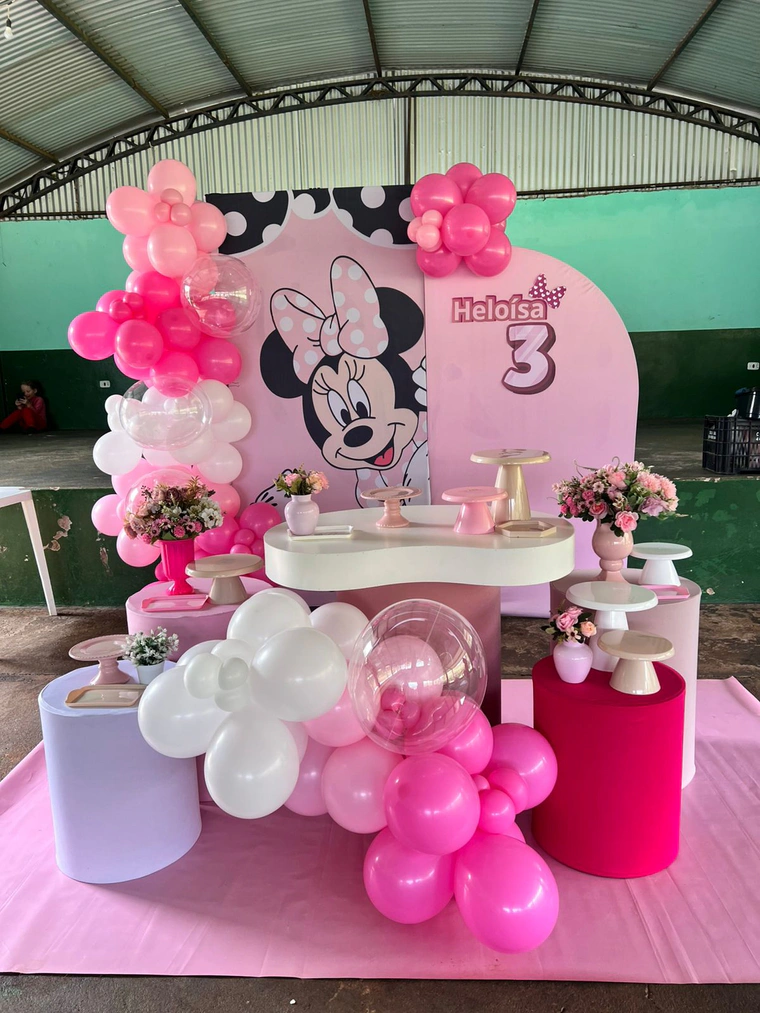 Painel da Minnie com balões rosa e branco, mesa curva branca e vasos de flores