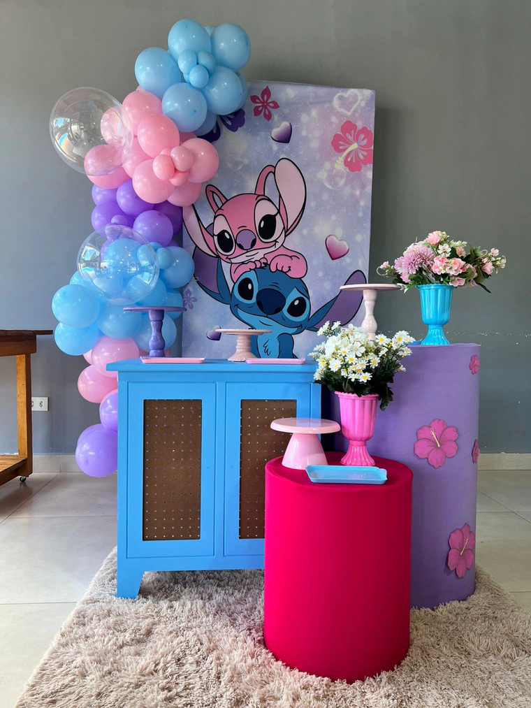 Painel do Stitch com arco de balões rosa, azul e lilás, e cilindros com flores de hibisco
